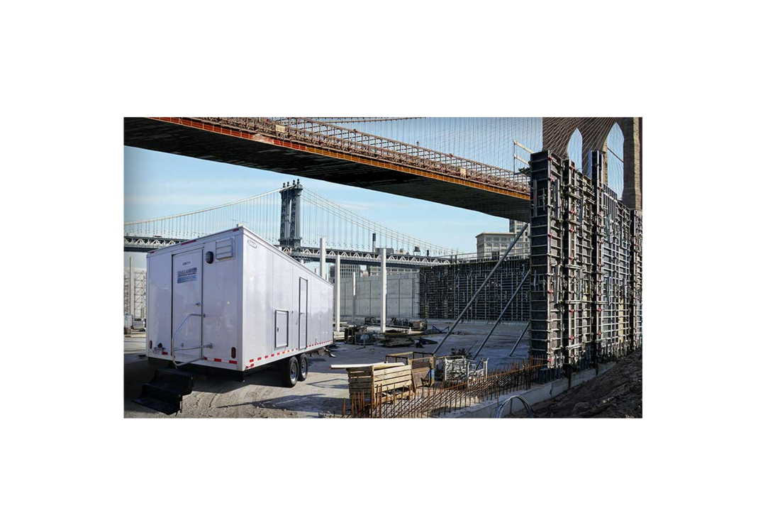 Decontamination trailer positioned at a bridge construction site, providing a controlled space for worker safety and compliance during blasting and industrial projects.